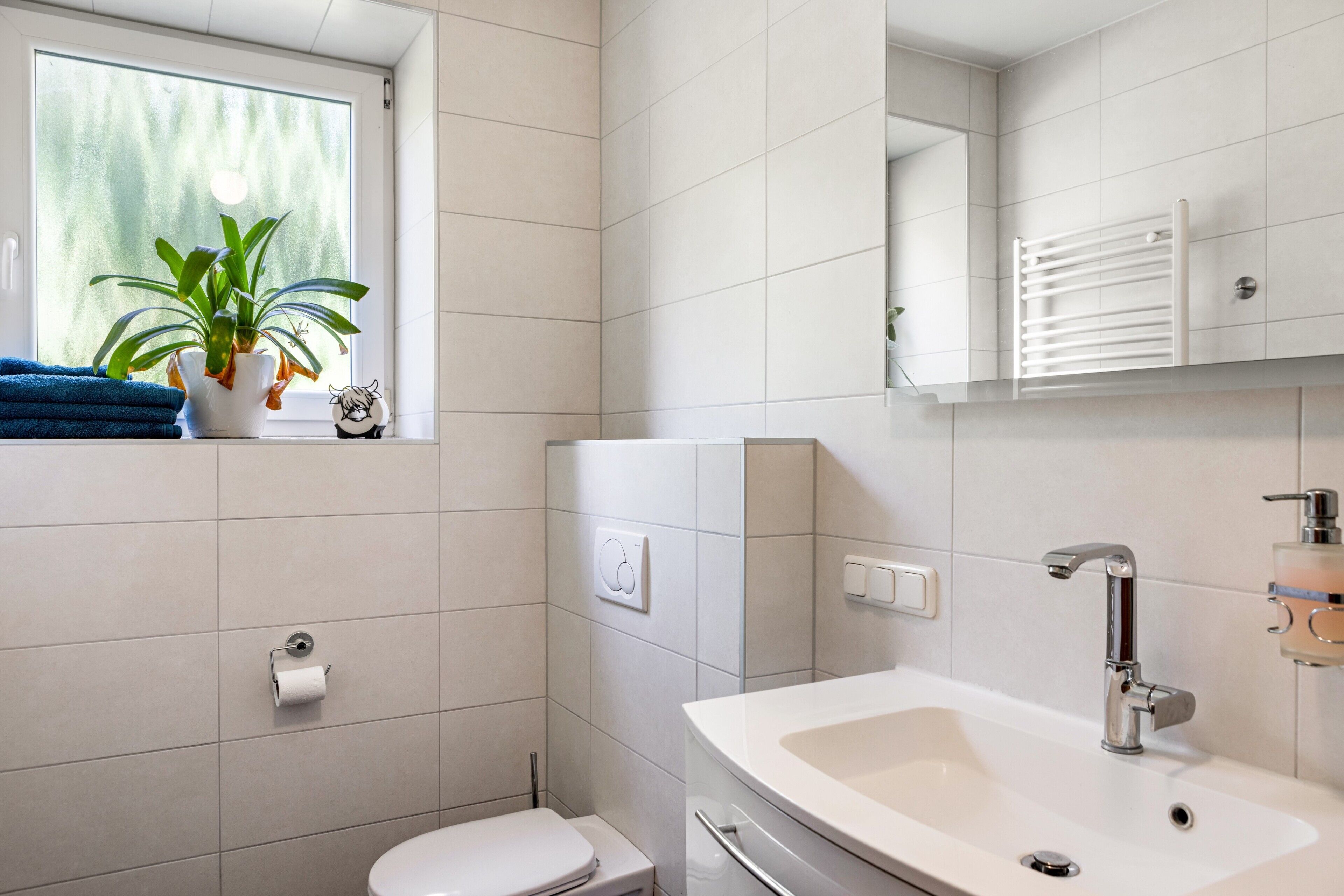 A modern bathroom with a toilet, sink, and a window with a plant.