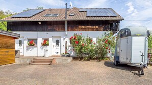 A two-story building with a solar panel roof, a white facade, and a small garden with red flowers. - Studio Apartment "Belroki Ranch" with Sauna, Terrace, and Garden (Waldeck)
