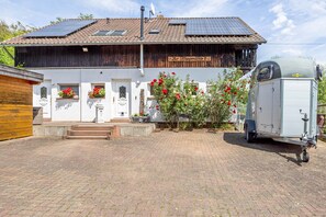 A two-story building with a solar panel roof, a white facade, and a small garden with red flowers. - Studio Apartment "Belroki Ranch" with Sauna, Terrace, and Garden (Waldeck)
