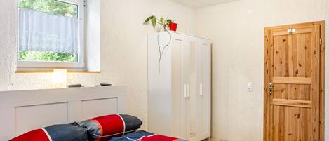 A bedroom with a bed, a wardrobe, a window with a curtain, and a door.