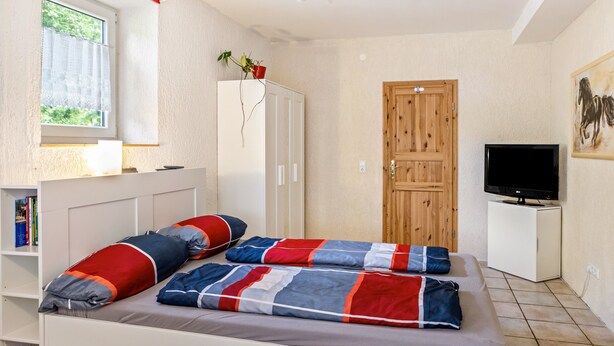 A bedroom with a bed, a television, a wardrobe, and a window. - Studio Apartment "Belroki Ranch" with Sauna, Terrace, and Garden (Waldeck)