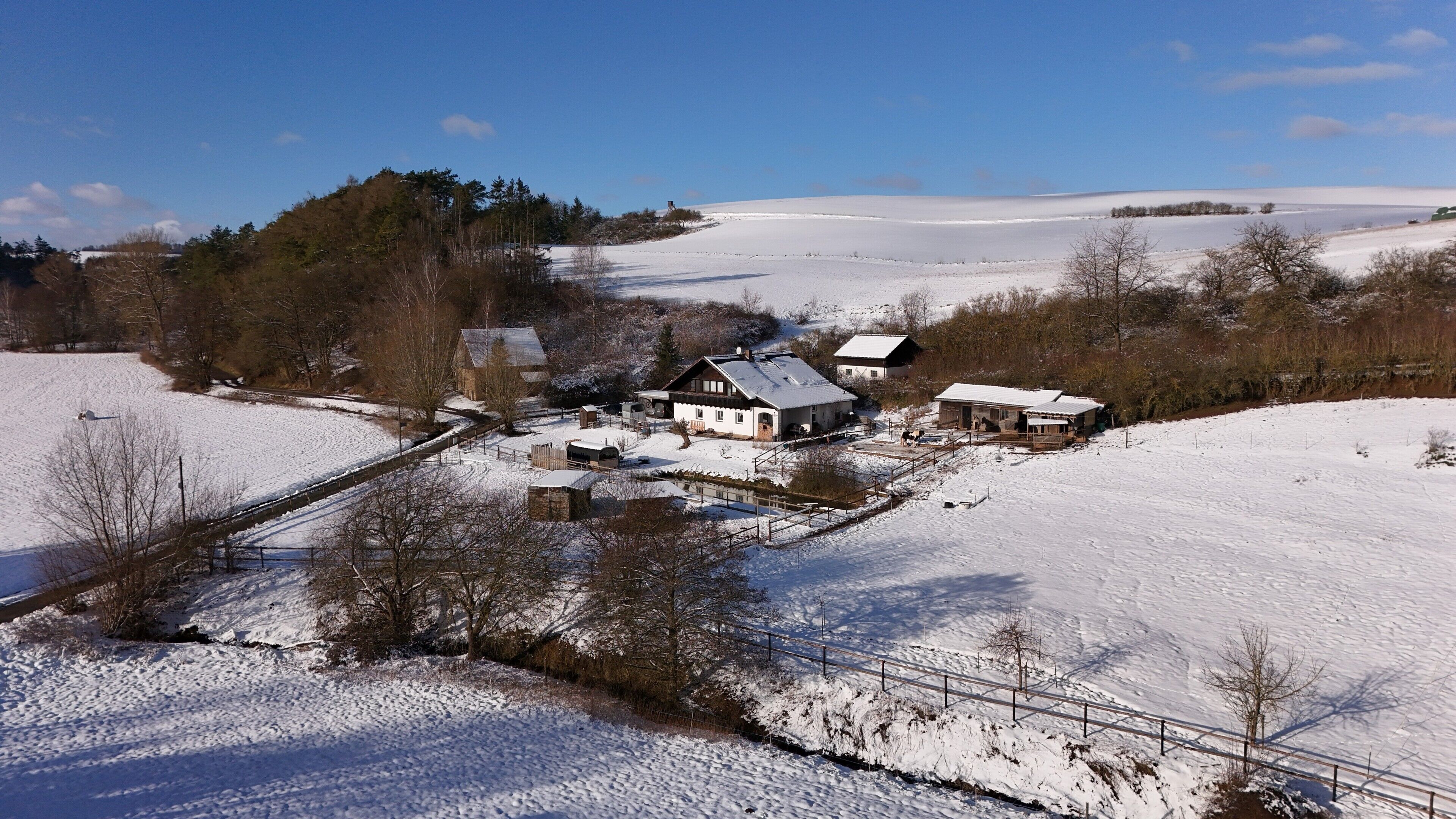 A rural landscape with snow-covered fields, a few buildings, and a clear sky.