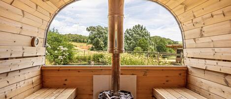 Una sauna con bancos de madera, una columna de calefacción central y vistas a la vegetación a través de un ventanal semicircular.