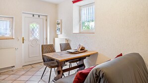 A room with a dining table, chairs, a sofa, a radiator, a door, and a window with a view. - Studio Apartment "Belroki Ranch" with Sauna, Terrace, and Garden (Waldeck)