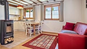 A cozy living area with a red sofa, a fireplace, a dining table with chairs, and a kitchen in the background. - Apartment "Pias Nature Retreat i - Studio" with Private Terrace, Shared Garden & Wi-Fi (Goppertsweiler)