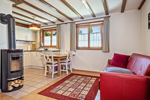 Un salon chaleureux avec un canapé rouge, une cheminée, une table à manger avec des chaises, et une cuisine en arrière-plan.