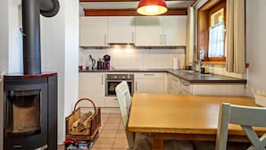 A kitchen with a wood-burning stove, white cabinets, a wooden dining table, and a window with curtains. - Apartment "Pias Nature Retreat i - Studio" with Private Terrace, Shared Garden & Wi-Fi (Goppertsweiler)