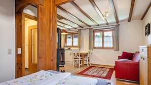 A room with a bed, a red sofa, a wooden ceiling, a kitchen area, and a window with curtains. - Apartment "Pias Nature Retreat i - Studio" with Private Terrace, Shared Garden & Wi-Fi (Goppertsweiler)