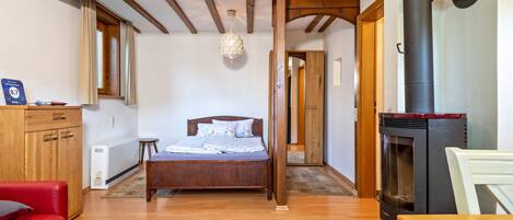 Un dormitorio con una cama de madera, un sofá rojo, una mesa de madera, una chimenea y una ventana con cortinas.
