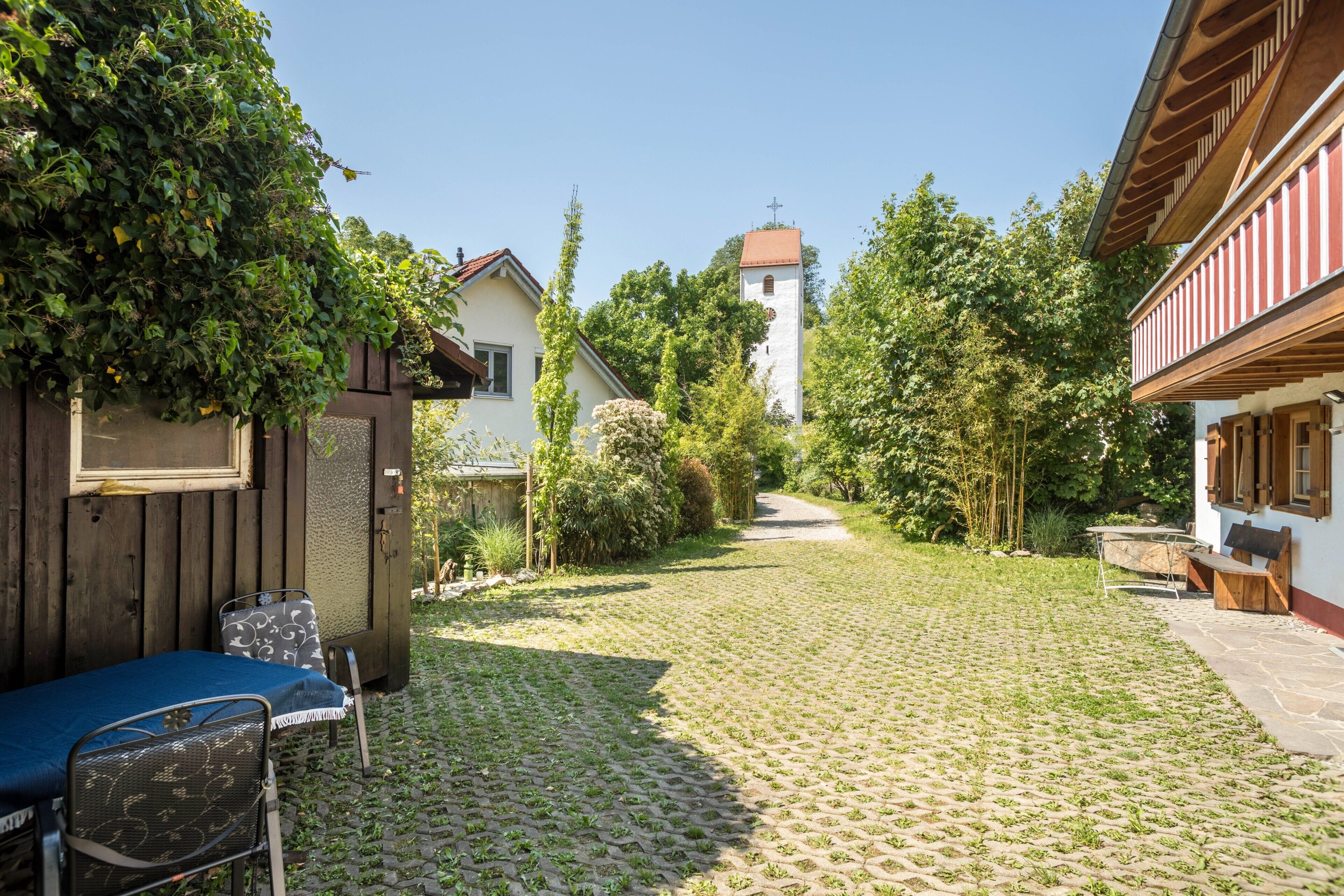 A cobblestone courtyard with a wooden bench, a metal chair, and a small table.