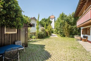 A cobblestone courtyard with a wooden bench, a metal chair, and a small table.