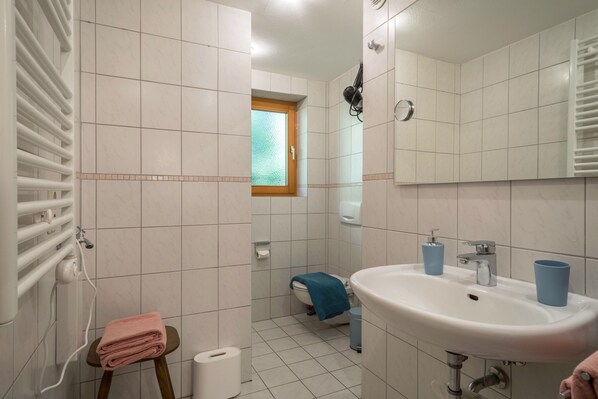 A bathroom with a white sink, a mirror, a towel rack, a window, and a toilet.