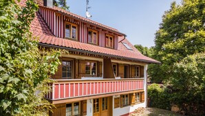 Un bâtiment à deux étages, doté d’un toit recouvert de tuiles rouges, de balcons en bois et d’une cour pavée.