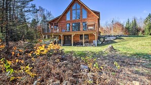 A large wooden cabin with a balcony, surrounded by trees and a grassy area. - Cozy & Peaceful Waterfront Cabin on Porter Lake! (New Vineyard)