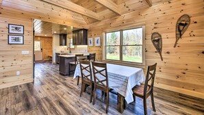 A wooden cabin interior with a dining area, kitchen, and large windows. - Cozy & Peaceful Waterfront Cabin on Porter Lake! (New Vineyard)