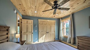 A bedroom with a wooden ceiling, a bed, a nightstand with a lamp, and a window with curtains. - Cozy & Peaceful Waterfront Cabin on Porter Lake! (New Vineyard)