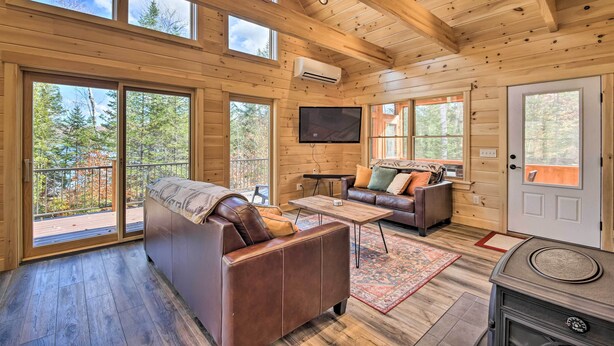 A log cabin interior with a large sliding glass door, a sofa, a coffee table, and a fireplace. - Cozy & Peaceful Waterfront Cabin on Porter Lake! (New Vineyard)