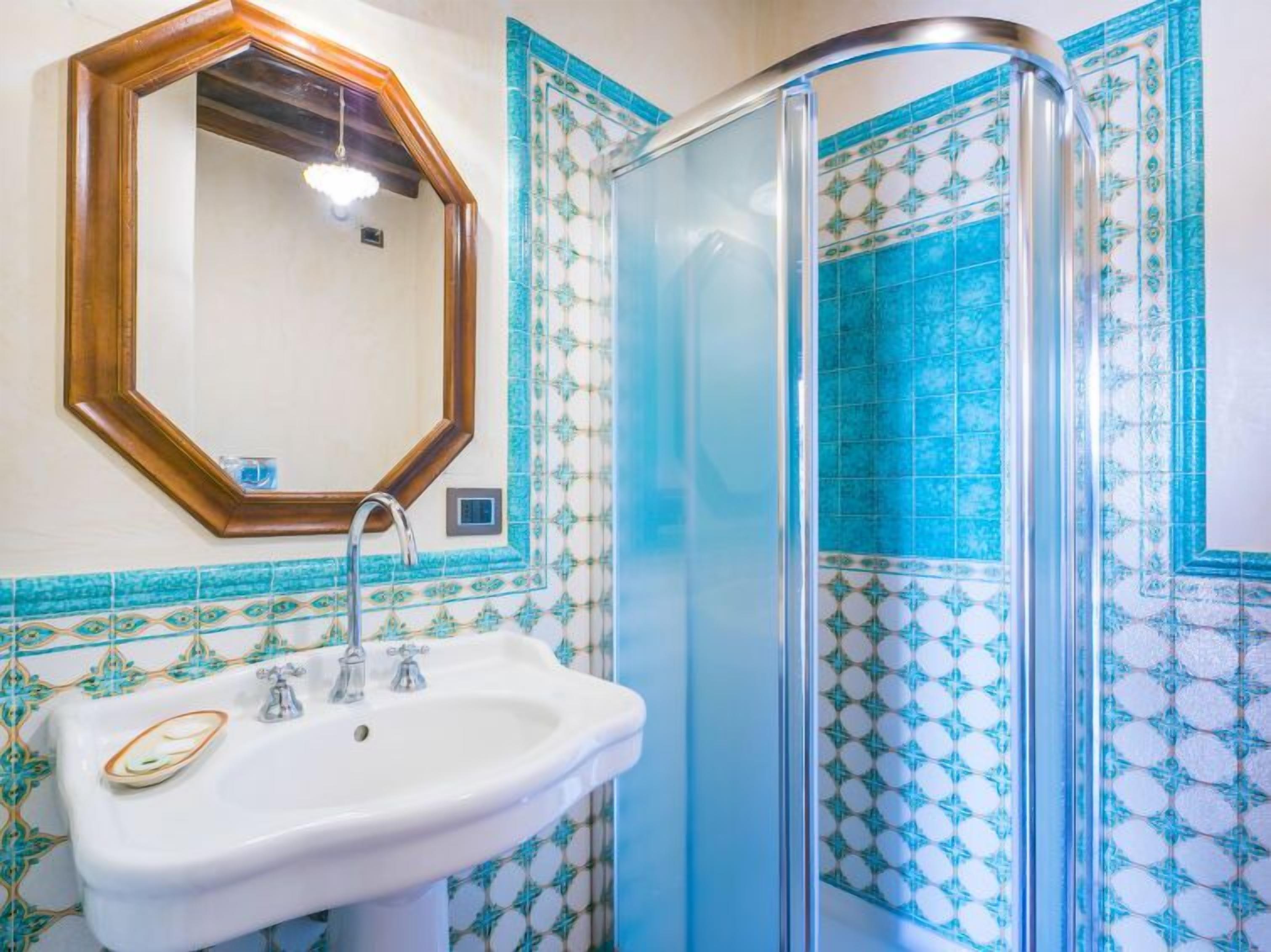 A bathroom with a white sink, a mirror, and a shower with blue patterned tiles.