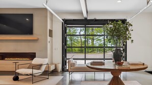 Una sala de estar moderna con chimenea, un televisor grande, una mesa de comedor con un florero y vistas a zonas verdes.