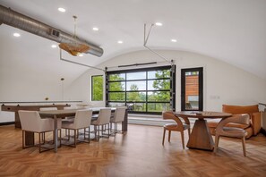 Una habitación amplia con techo alto, ventanas grandes y un comedor con sillas y mesas.
