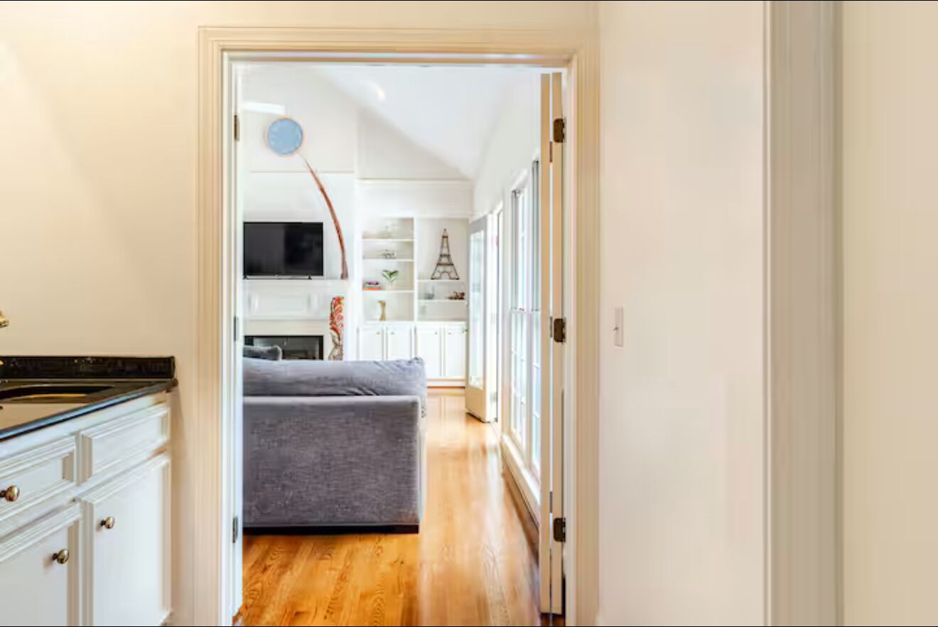 Un couloir étroit avec un canapé gris, des meubles blancs et un plancher en bois.