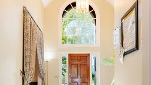 A hallway with a wooden door, a chandelier, and a view of greenery outside. - 5000Sqft MassiveHome,5.5Bath,Pool,HotTub,Mins to CopperCreekTennis, Fort-Benning (Columbus)