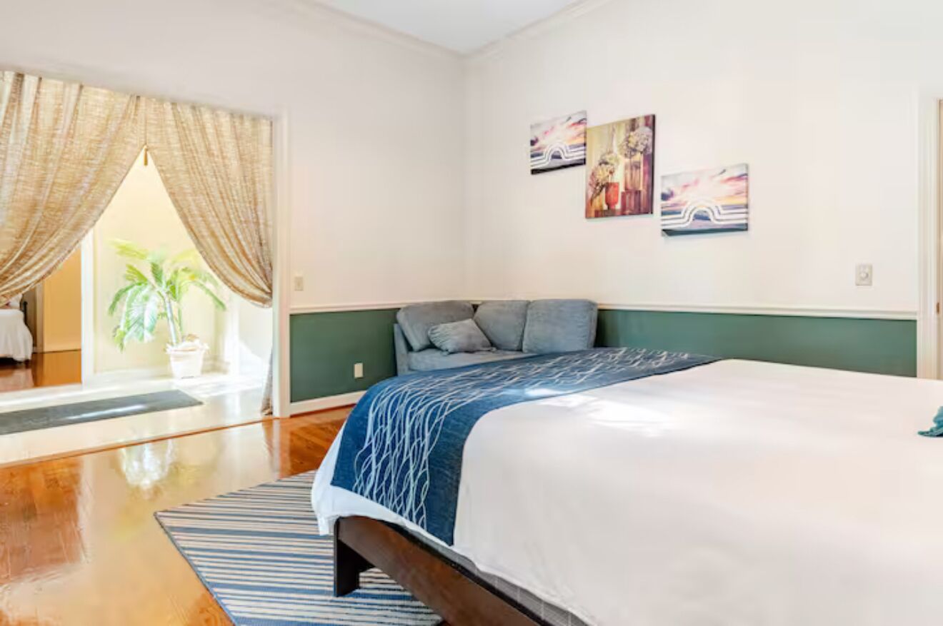 A bedroom with a bed, a window with curtains, and wall art.