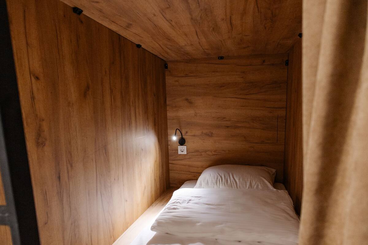 A small, single-bed room with wooden walls and a simple, functional design.