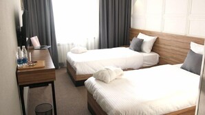 Habitación de hotel con dos camas, cabecera de madera, escritorio con una computadora portátil y un pequeño cesto de basura.