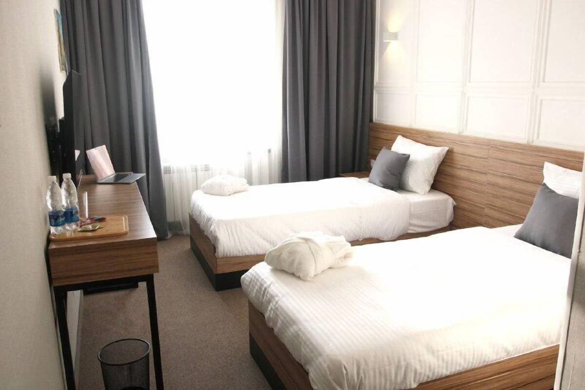 A hotel room with two beds, a wooden headboard, a desk with a laptop, and a small trash bin.