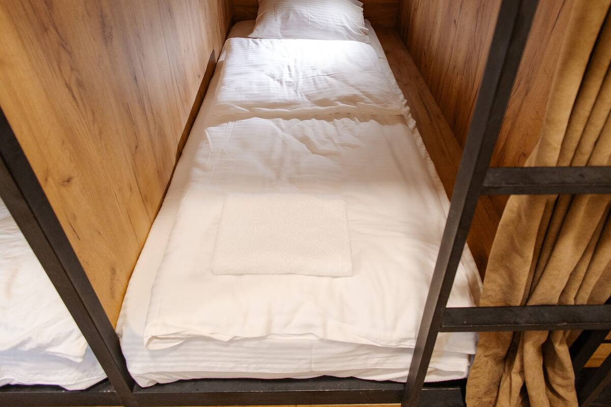 A small, wooden room with a bunk bed, a single light fixture on the wall, and a wooden floor.