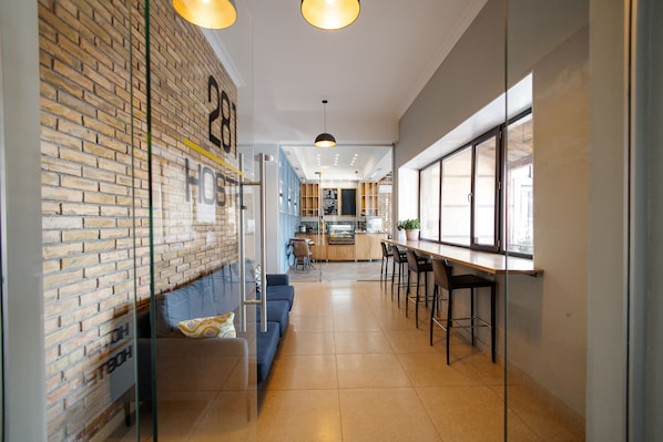 A modern interior with a brick wall, a seating area with a sofa and chairs, a bar with stools, and a kitchen area in the background. - 281 Hotel & Hostel (Bishkek)