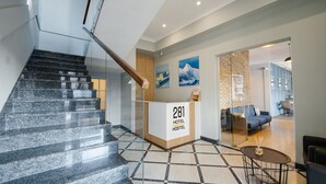 Zona de recepción de hotel con una escalera, mostrador de recepción que dice "281 HOTEL HOSTEL" y un área de estar con mesa y sillas.