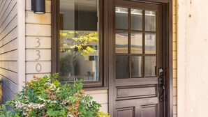 Hausnummer 330, eine braune Haustür mit Fenster und ein kleiner, grüner Busch davor.