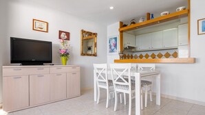 Ein modernes Wohnzimmer mit Flachbildfernseher, einer Kommode, einem Esstisch mit Stühlen, einem Spiegel und einem Regal mit Dekoration.