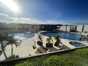 Un'area piscina con diverse piscine, palme e cielo sereno.