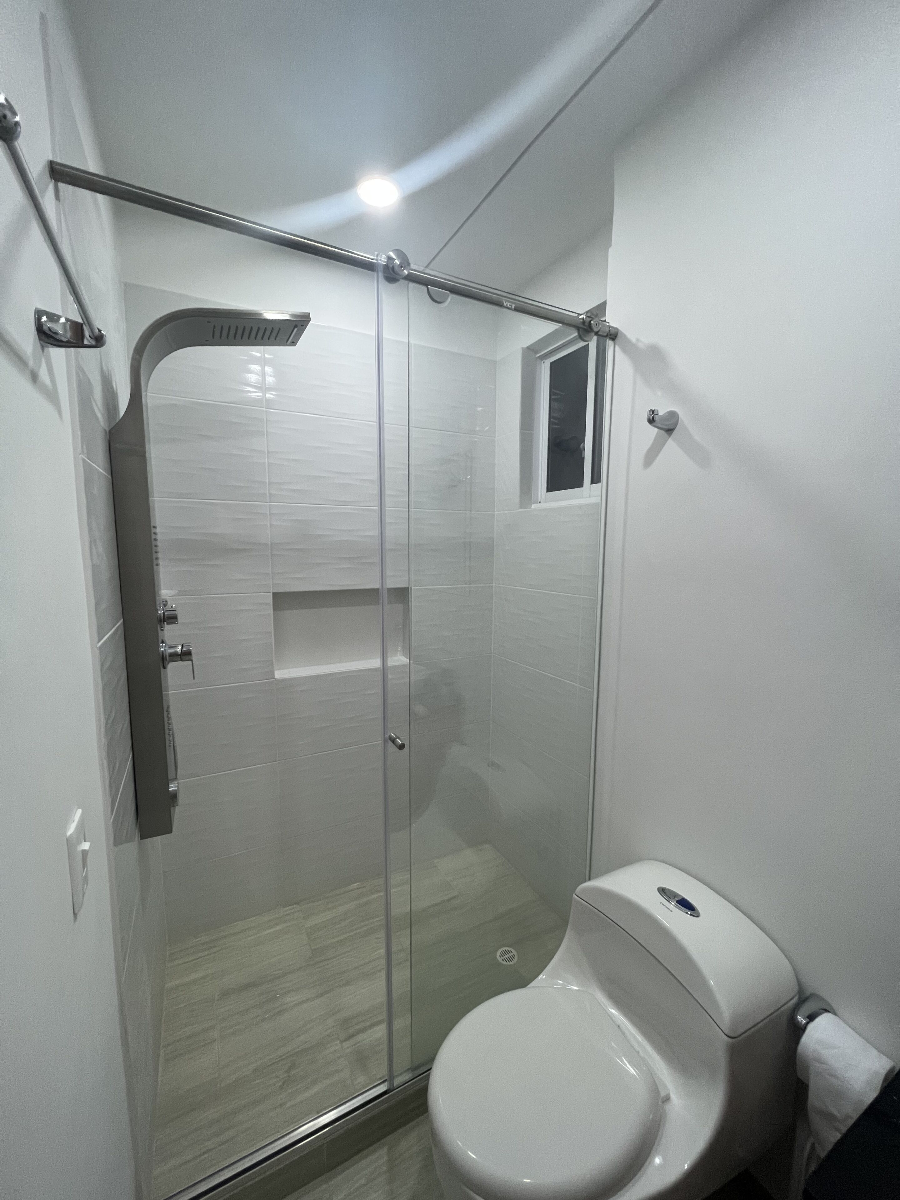 A modern bathroom with a glass-enclosed shower, a toilet, and a small window.