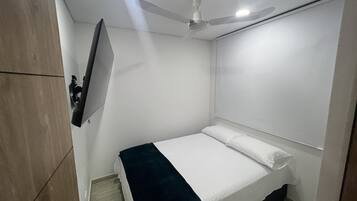 Ein Schlafzimmer mit Bett, Deckenventilator, montiertem Fernseher und Holzschrank.