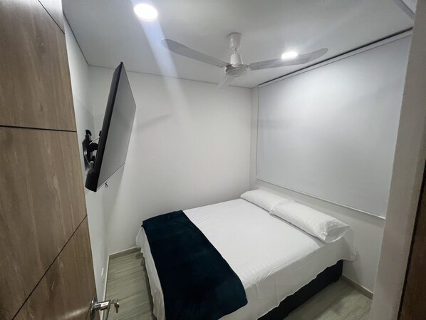 A bedroom with a bed, a ceiling fan, a mounted TV, and a wooden wardrobe.