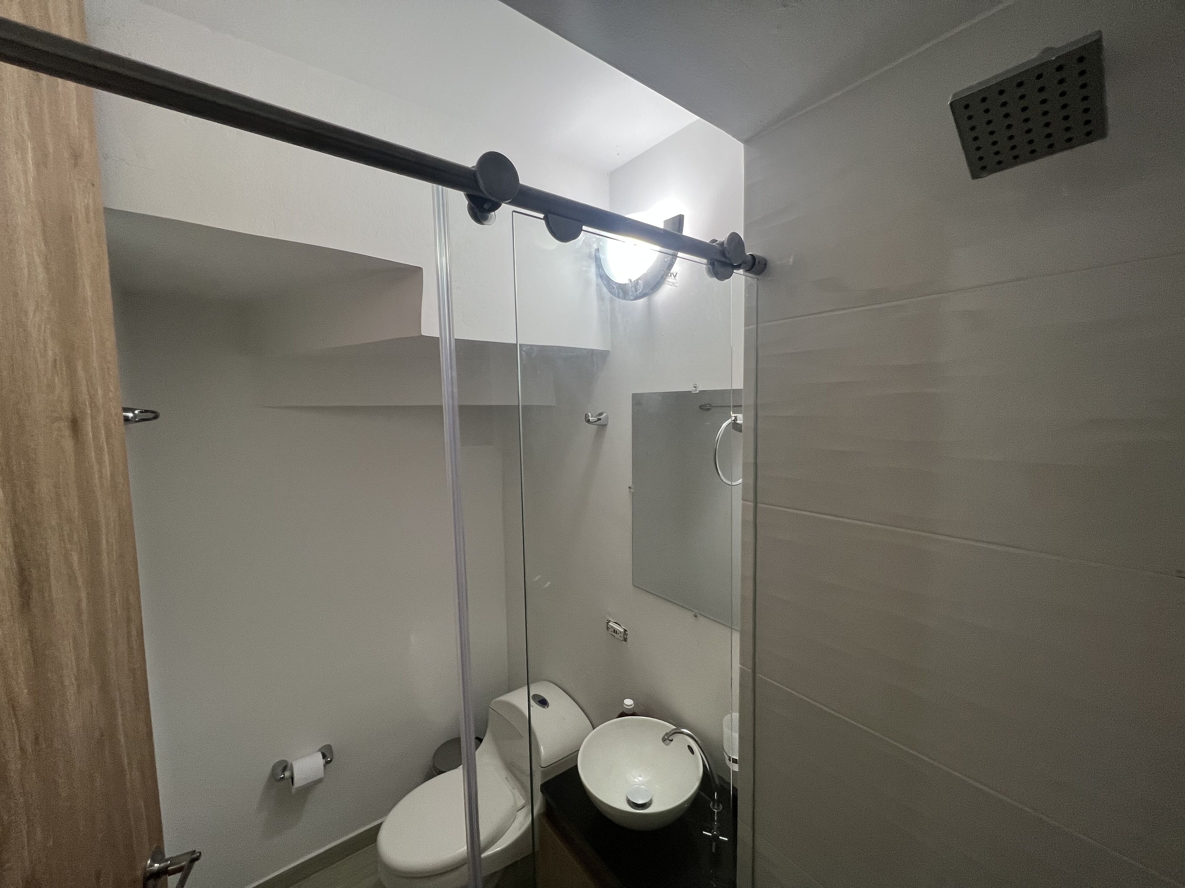 A small, modern bathroom with a toilet, sink, and glass shower enclosure.