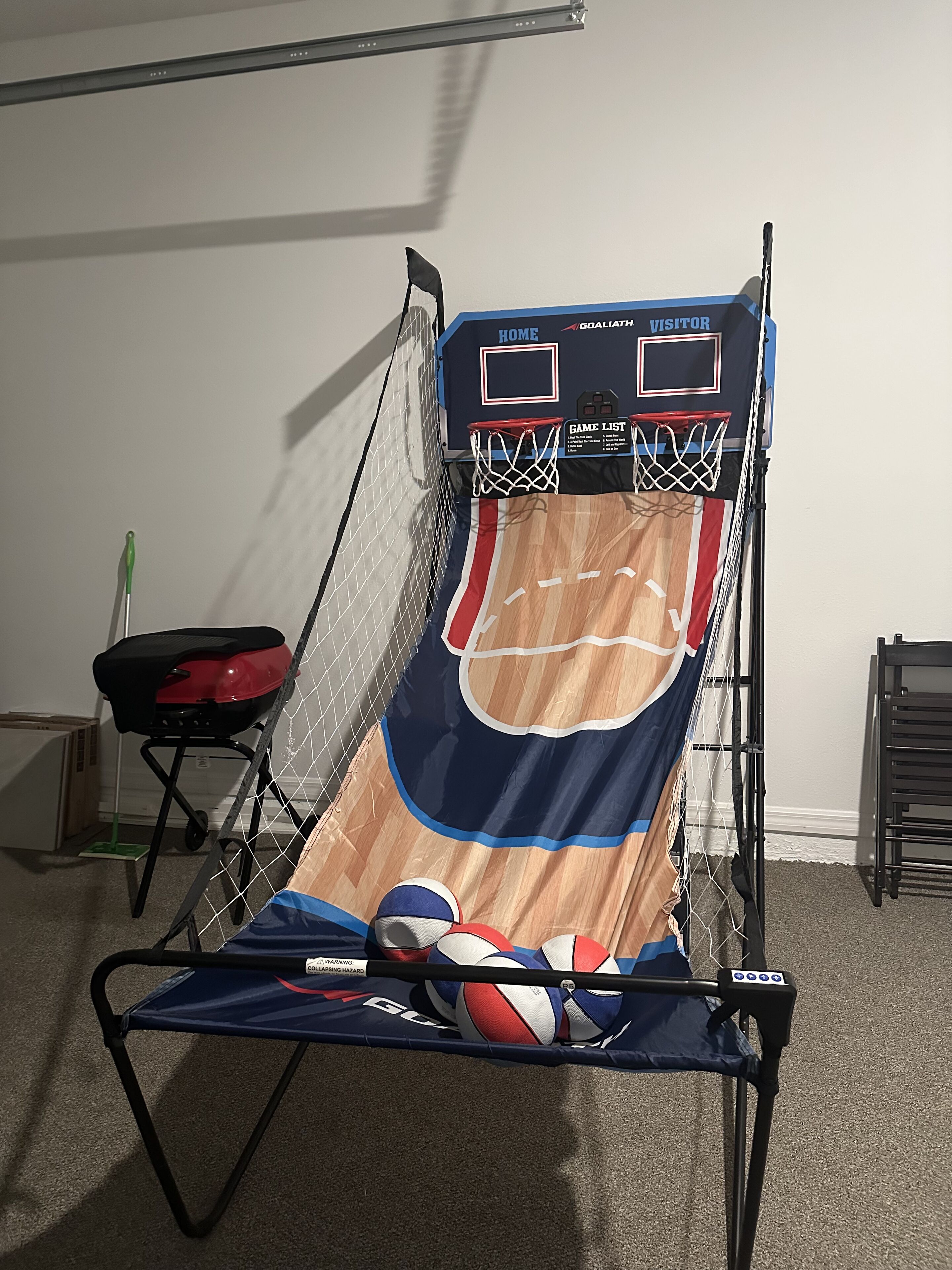 Een basketbalring met net, een rode barbecue en een blauwe klapstoel.