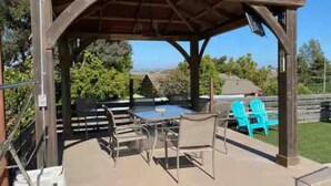 An outdoor patio with a covered seating area, a table, and chairs. - Oceanside Gem W/ Pool, Hot Tub and Game Room! (Oceanside)