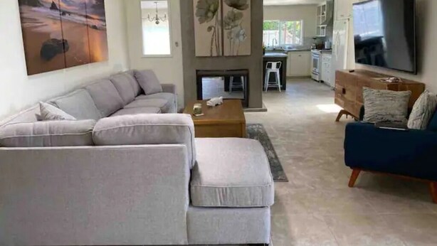 A living room with a grey sectional sofa, a blue armchair, a coffee table, and a fireplace. - Oceanside Gem W/ Pool, Hot Tub and Game Room! (Oceanside)