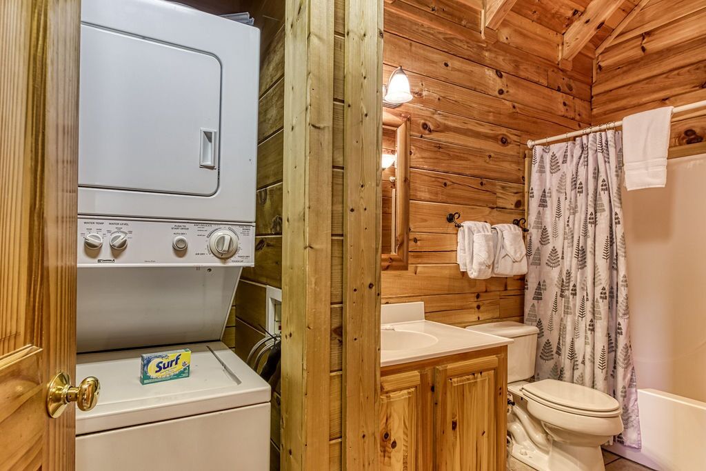 A compact wooden cabin with a washing machine, a sink, and a toilet.