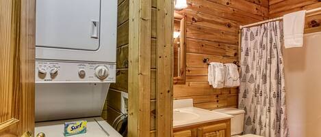 A compact wooden cabin with a washing machine, a sink, and a toilet.