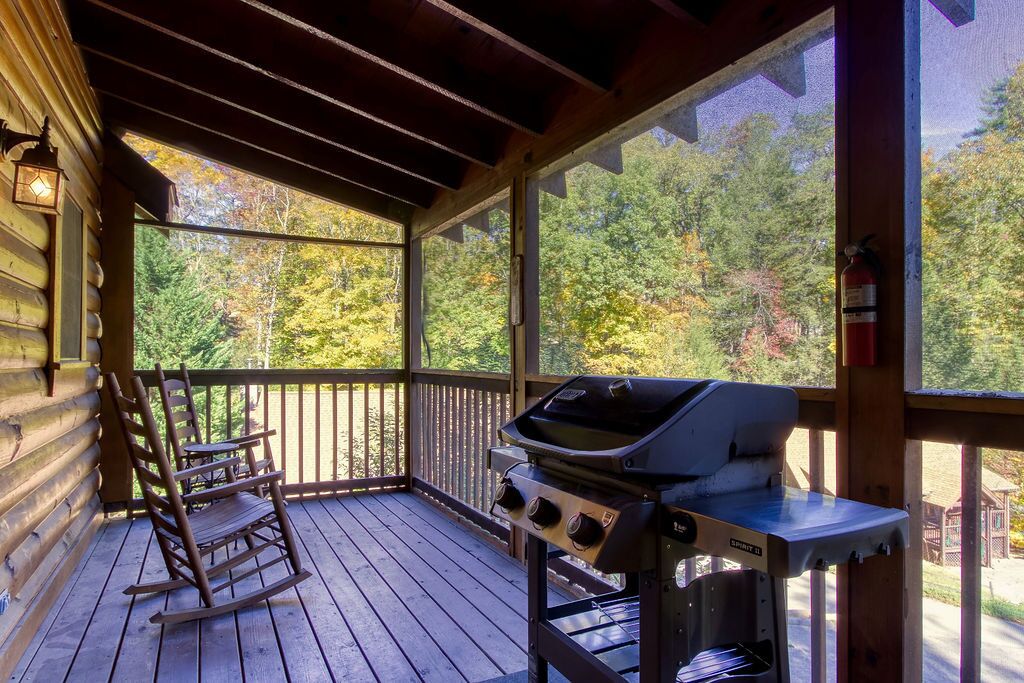 A wooden deck with a grill and a rocking chair, overlooking a forested area.