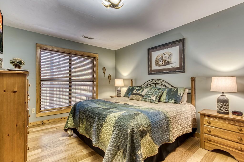 A bedroom with a bed, wooden dresser, and a window with blinds.