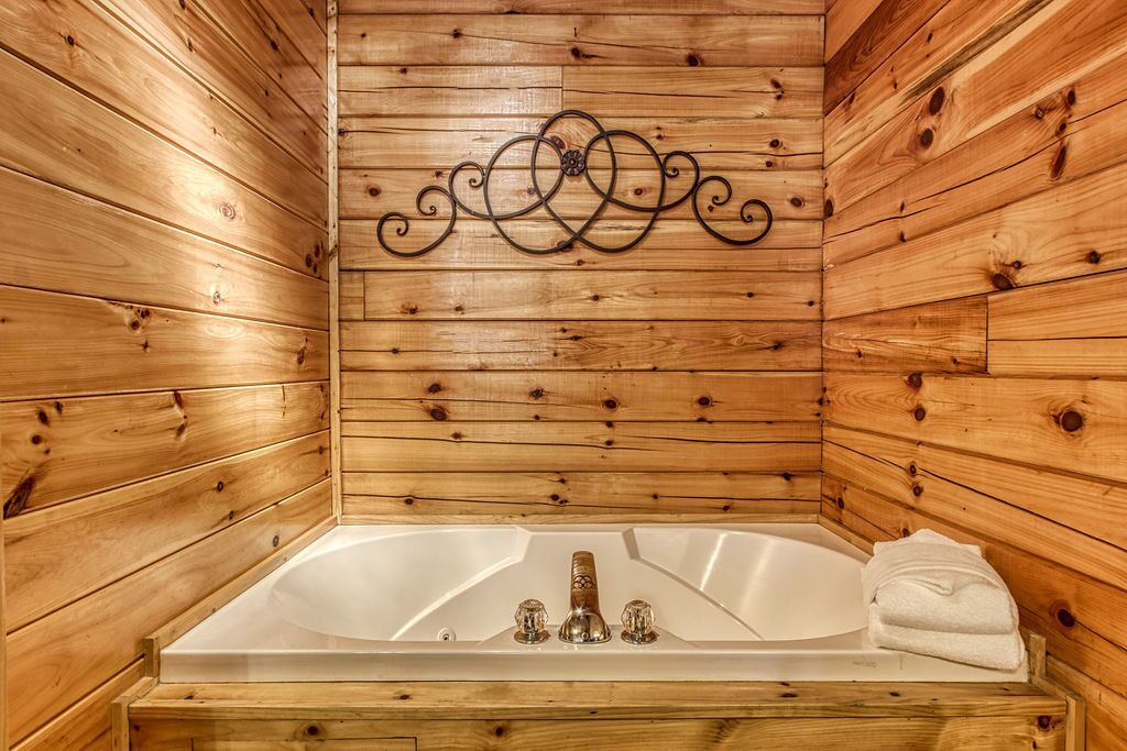 A wooden cabin with a large bathtub, wooden walls, and a decorative metal piece above the tub.