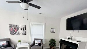 Un soggiorno moderno con ventilatore a soffitto, camino, televisione e un quadro appeso al muro.