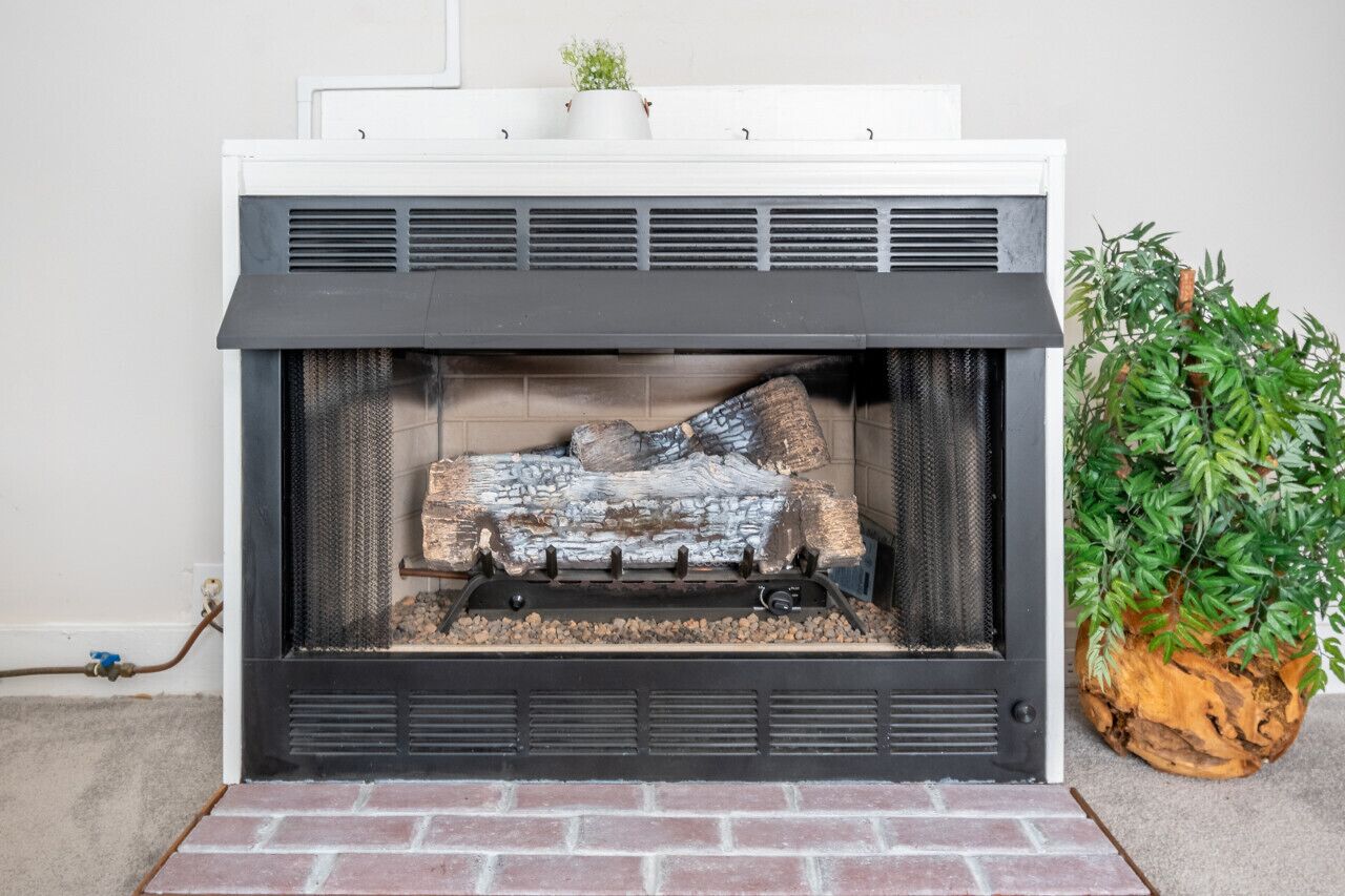A fireplace with a white mantel, a log fire, and a potted plant beside it.